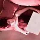 Attractive model lays on couch with computer.