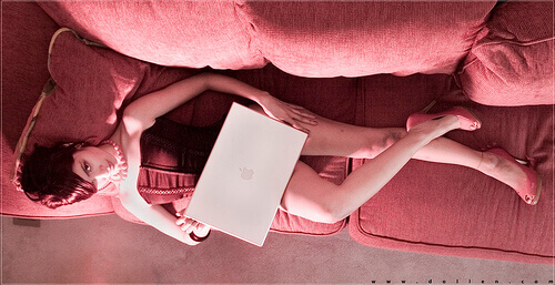 Attractive woman lays on sofa with computer.