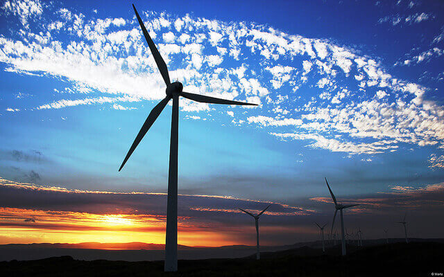 A wind turbine appears over a sunset horizon.