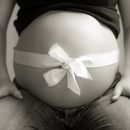A bow is wrapped around the belly of a pregnant woman as if it were a present.