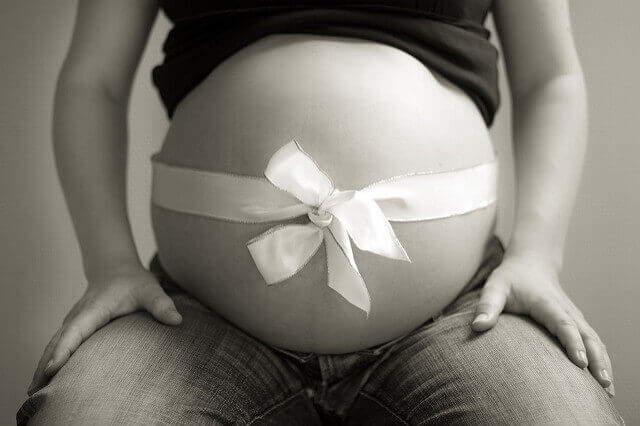A bow is wrapped around the belly of a pregnant woman as if it were a present. 