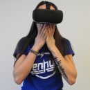A woman wearing a VR headset covering her mouth in what looks like shock.