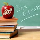 An apple with male and female symbols carved into it appears in front of a chalkboard that says "Sex Education."