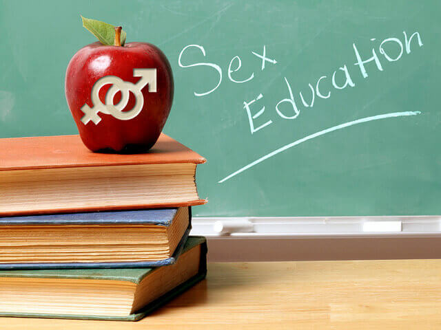 An apple with male and female symbols carved into it appears in front of a chalkboard that says "Sex Education."