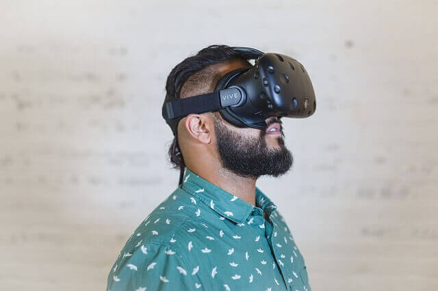 A bearded man with a green shirt wears a VR headset. 