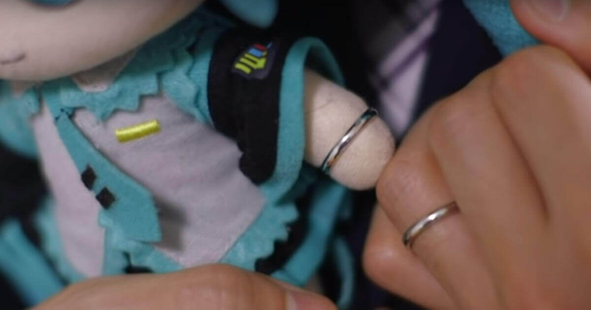 A man's hand and the hand of a stuffed animal are both shown wearing wedding rings.