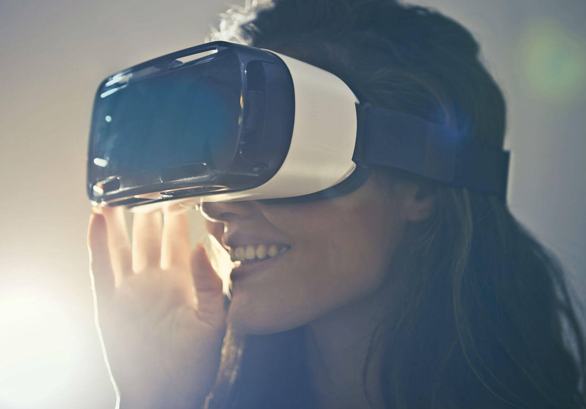 A caucasion woman smiles as she dons a white and black VR headset