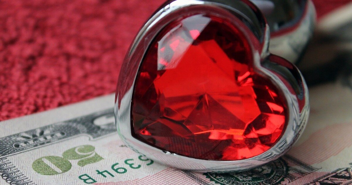 A red and sliver heart-shaped sex toy lies on a US$50 bill ontop of red fabric.