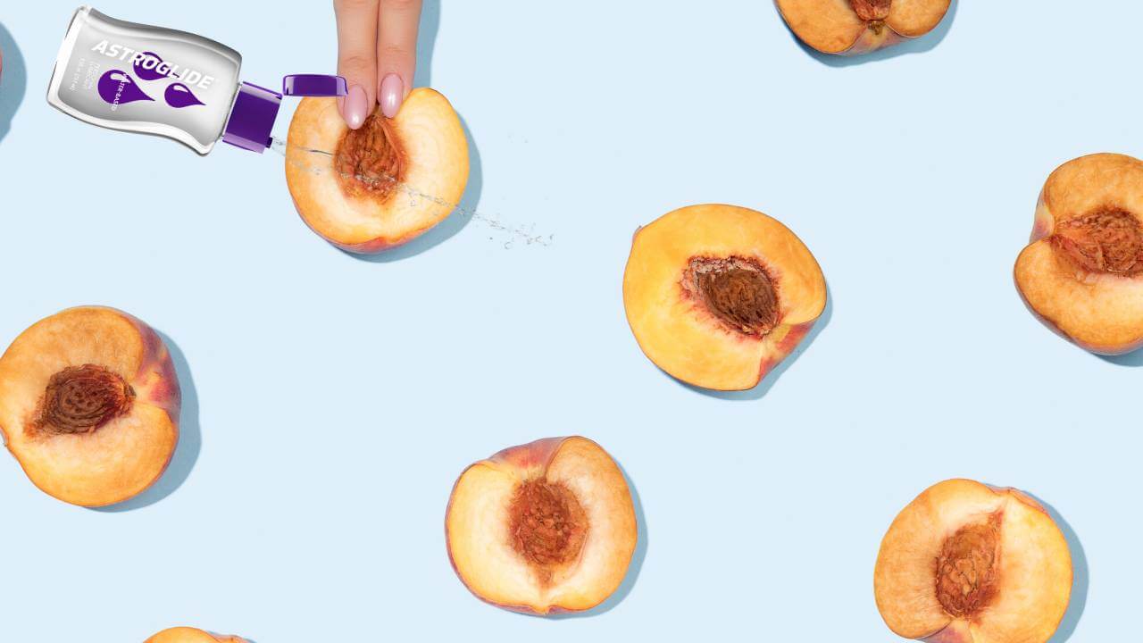 Halved and pitted peaches appear on a blue background next to Astroglube and a pair of fingers. 