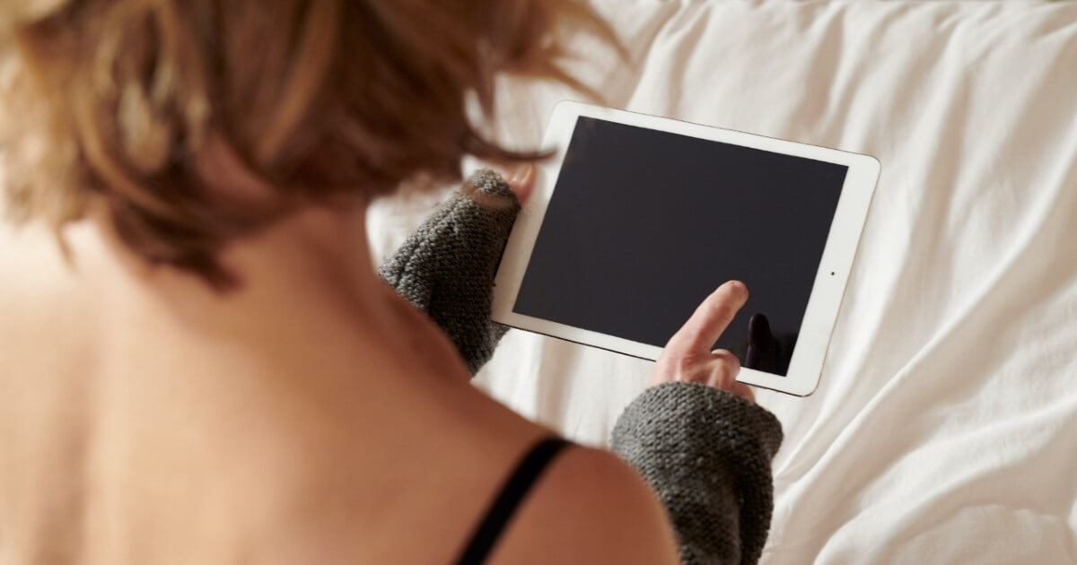 A woman holds a tablet while sitting in bed.