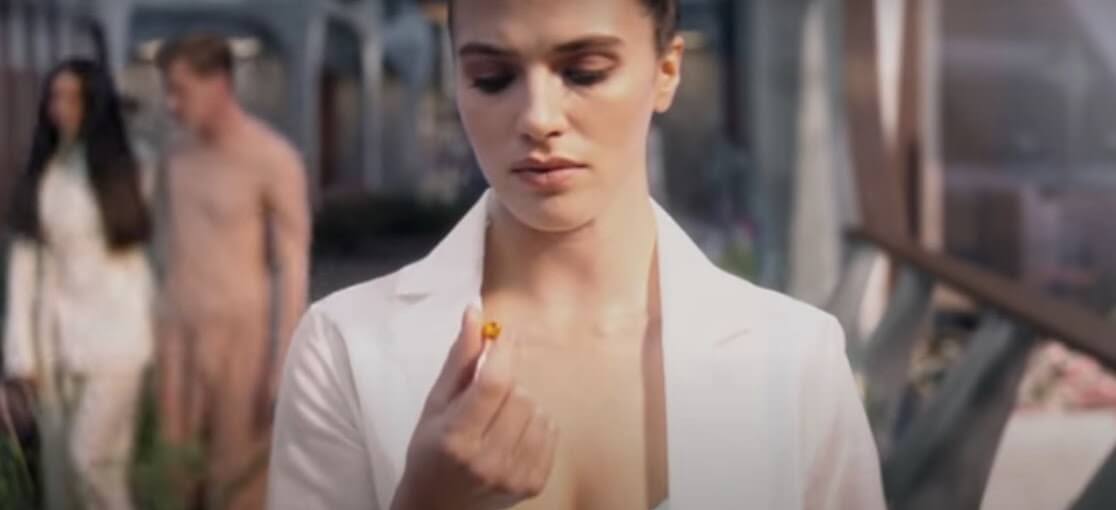 A young woman wearing white looks down at a pill.