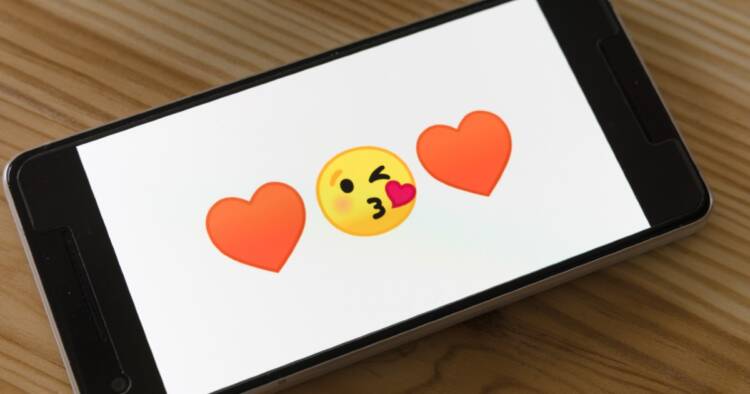 A smartphone shows two heart emojis with a yellow-face kiss emoji in the middle.