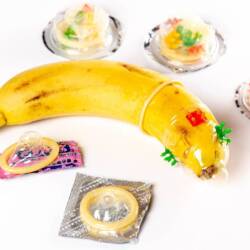 A banana is shown weraing a condom with various unopened condoms lying around it.