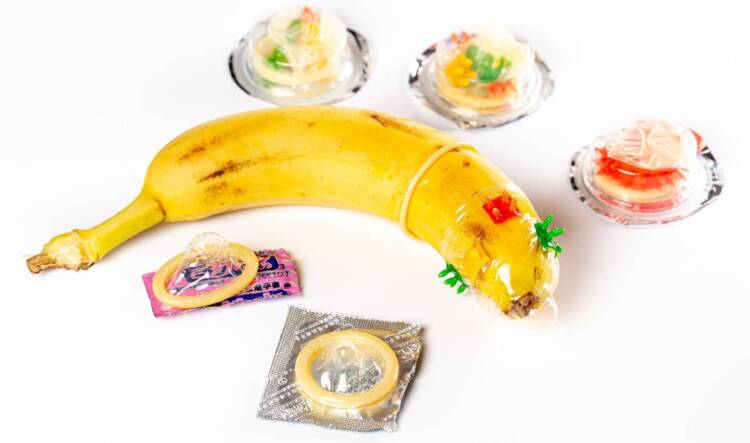 A banana is shown weraing a condom with various unopened condoms lying around it.