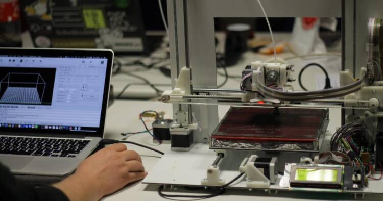 Image of a man working on laptop and 3D printer