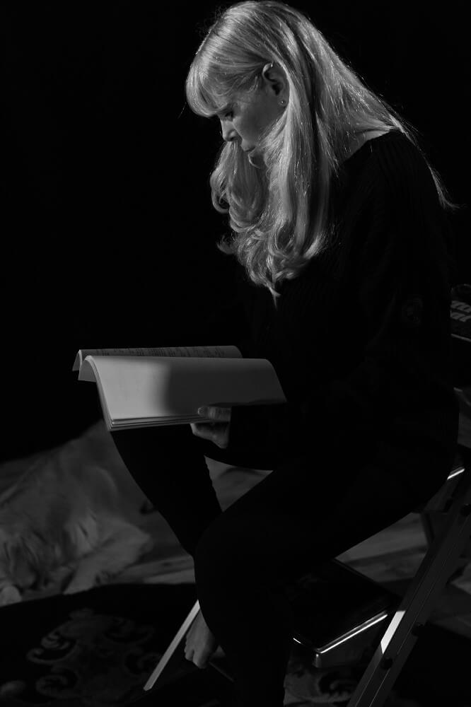 Black and white photo of Sssh founder Angie Rowntree sitting on ladder and reading book