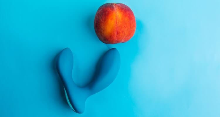 Prostate massager sex toy near a peach representing a butt for anal masturbation. Blue background.