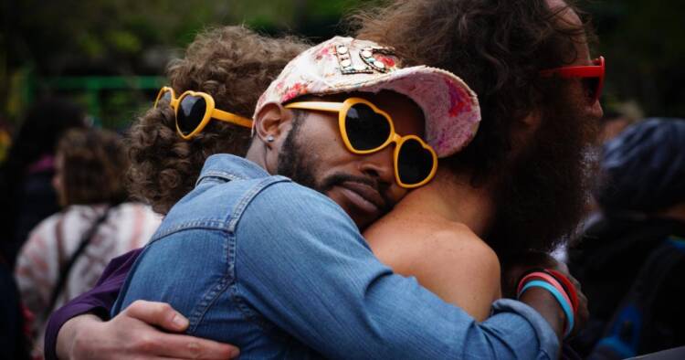 A picture of men wearing yellow, heart shape sunglasses; hugging each other