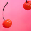 Two red cherries on a pink background.