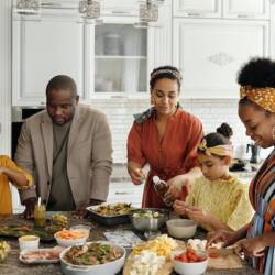 A family with four adults making dinner together with two children.