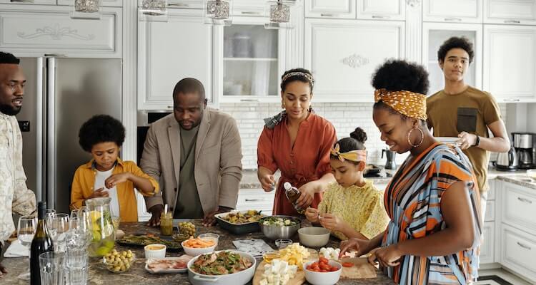 A family with four adults making dinner together with two children.