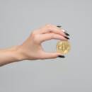Hand with long nails holding a physical Bitcoin.