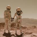 Two astronauts in space suits looking out into the distance and holding hands.