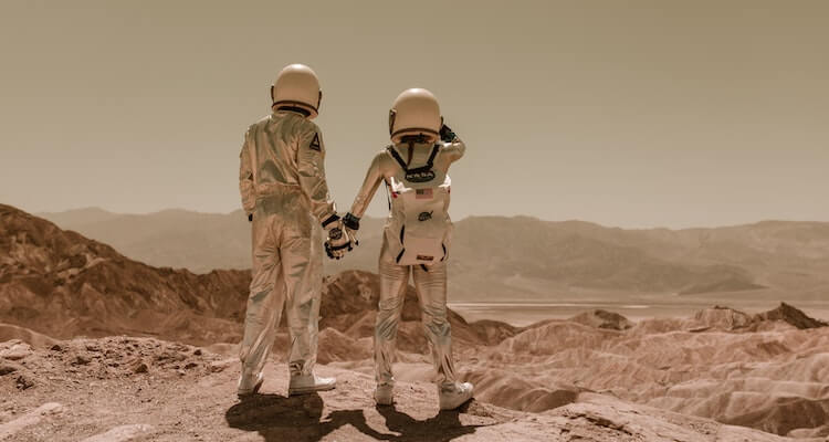 Two astronauts in space suits looking out into the distance and holding hands.