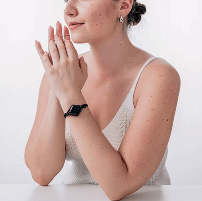 A woman sitting and wearing the Bellabeat Ivy product as a bracelet. 