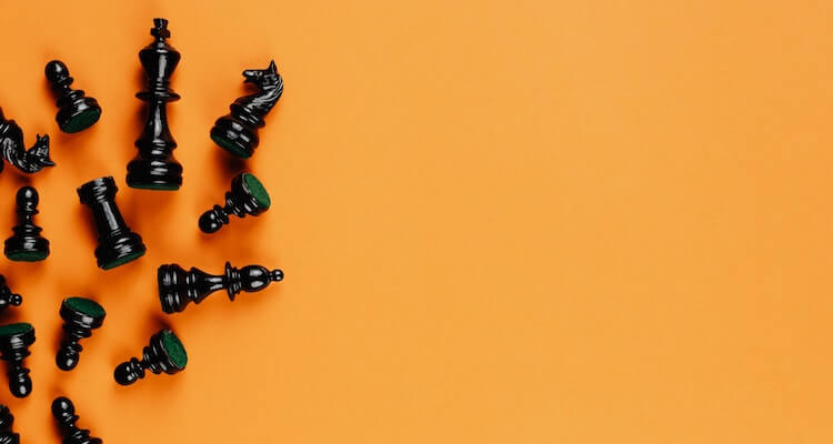 Black chess pieces laying across an orange background.